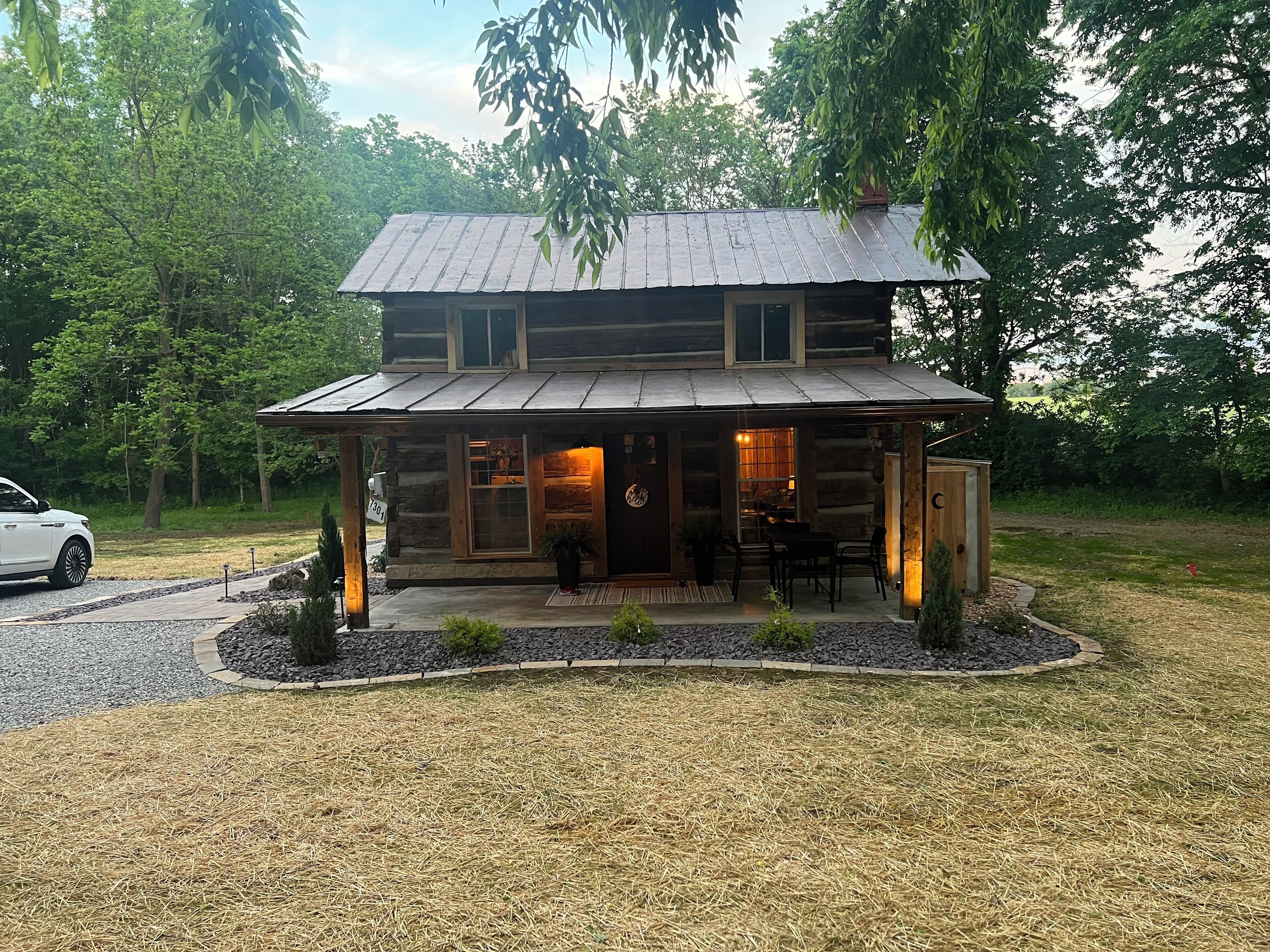 A log cabin with a covered porch, a driveway, and a surrounding wooded area.