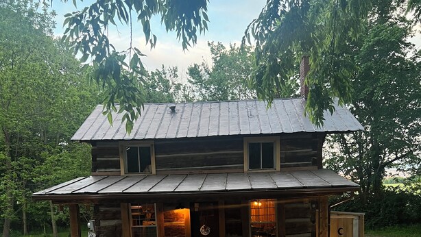 Une cabane rustique en rondins de bois, dotée d’un porche abrité et d’une cheminée en pierre.