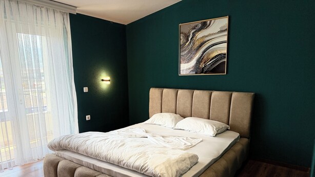 A bedroom with a bed, a wall-mounted light, and a painting. - Lindi Premium Hotel (Prizren)