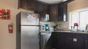 Une cuisine avec des meubles de couleur sombre, des appareils en acier inoxydable et un extincteur fixé au mur.