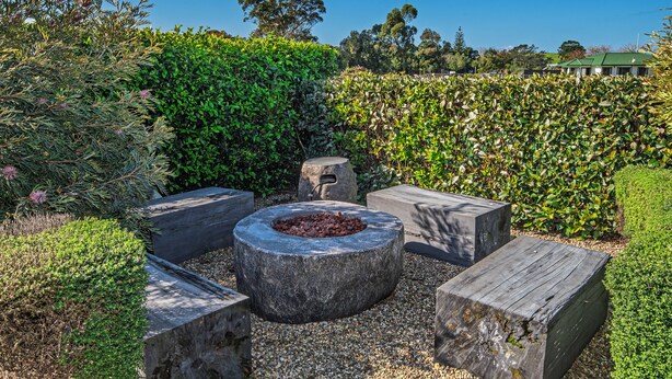 A garden area with a circular stone fire pit surrounded by wooden benches.