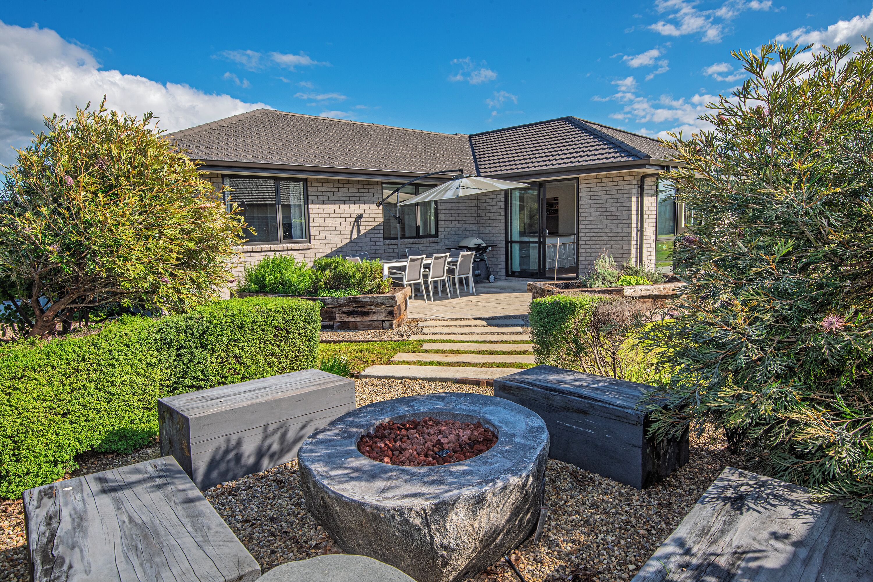 A modern house with a patio area featuring a fire pit, outdoor seating, and a well-maintained garden.