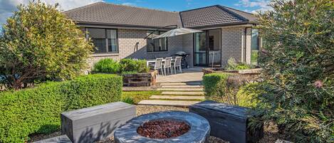 A modern house with a patio area featuring a fire pit, outdoor seating, and a well-maintained garden.