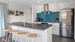 A modern kitchen with a central island, bar stools, stainless steel appliances, and teal backsplash tiles.