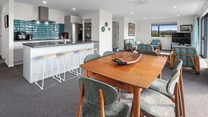 A modern kitchen with a central island, bar stools, and a dining area with a wooden table and cushioned chairs.