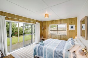 Un dormitorio con un amplio ventanal corredera a un jardín, una cama con colcha estampada y un panel de pared de madera.