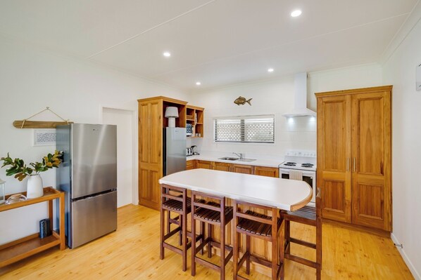 Una cocina moderna con armarios de madera, un refrigerador de acero inoxidable, una encimera blanca y un conjunto de taburetes de bar de madera.
