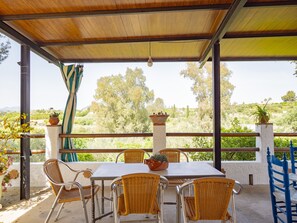 Un espace extérieur aménagé, abrité et doté de tables et de chaises, de plantes en pot, et offrant une vue sur le paysage environnant.
