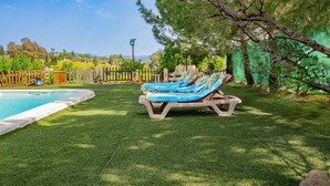 A poolside area with a wooden fence, a view of the countryside, and a large tree.