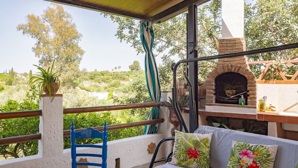 A balcony with a view of a hilly landscape, a brick oven, and a blue chair.