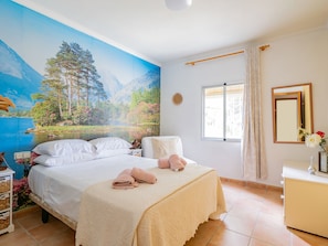 Une chambre à coucher avec un grand lit, une fenêtre avec des rideaux, une table de chevet et un miroir fixé au mur.