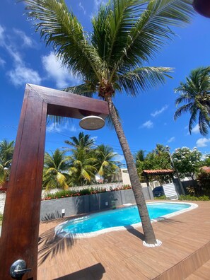 Une structure de pergola en bois avec un espace de détente circulaire, une piscine et des palmiers.
