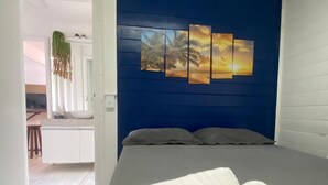 Une chambre à coucher avec un lit, un mur d’accent bleu et un tableau représentant un coucher de soleil.