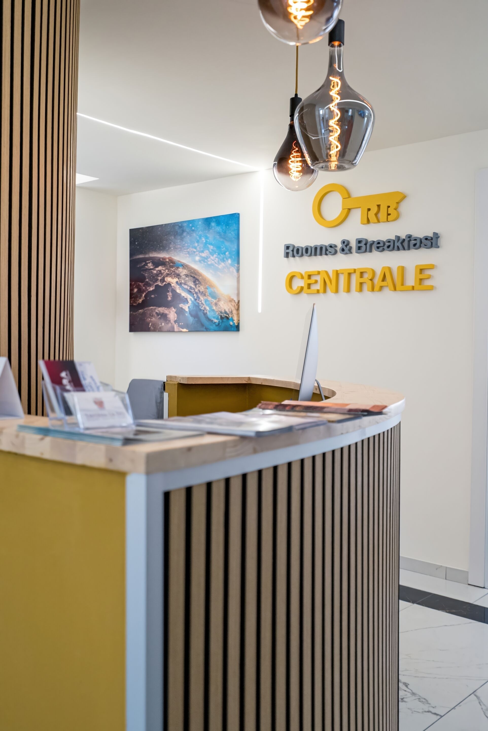 A reception desk with a modern design, a wall sign for 'Rooms & Breakfast CENTRALE', and a large painting of a night sky.