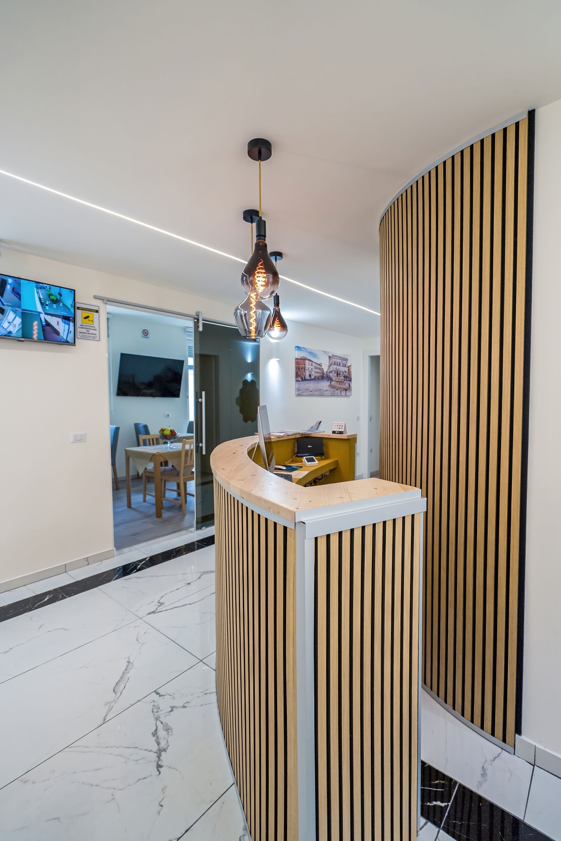 Un área de recepción con un mostrador de madera, una lámpara colgante moderna y un televisor de pantalla plana en la pared.