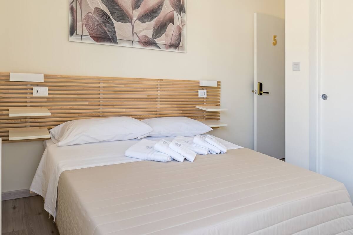 A neatly made bed with a beige quilt, a wooden headboard, and a wall-mounted artwork above it.