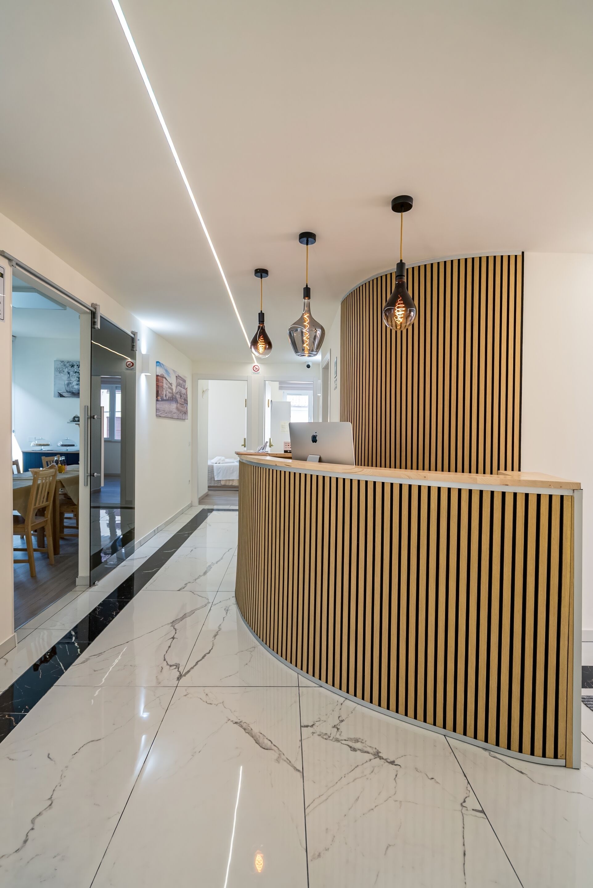 Una zona de recepción moderna con un mostrador curvo de madera, suelo de mármol e iluminación colgante.