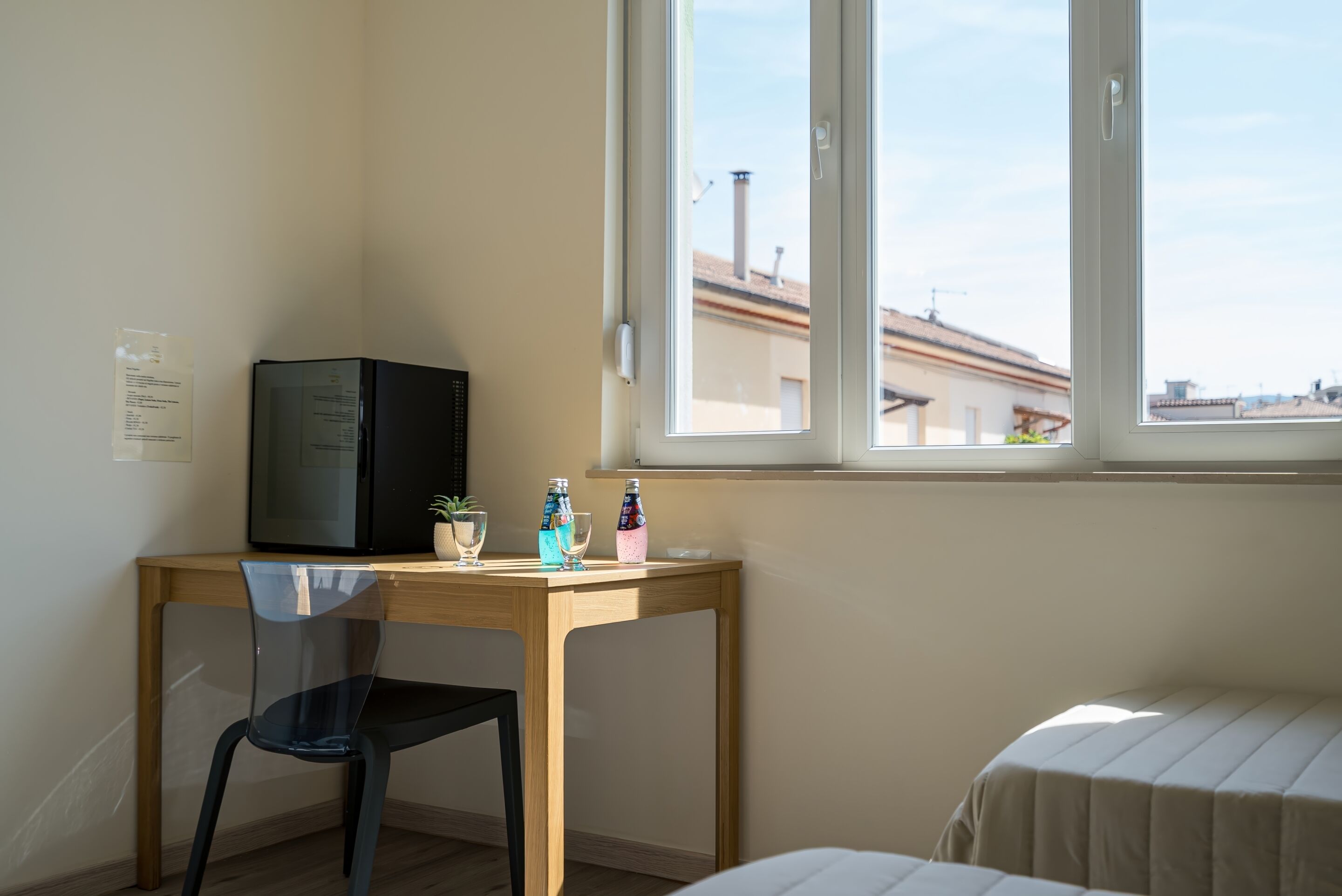 Una habitación con un escritorio de madera, una silla, una cama y una ventana con vista a edificios.