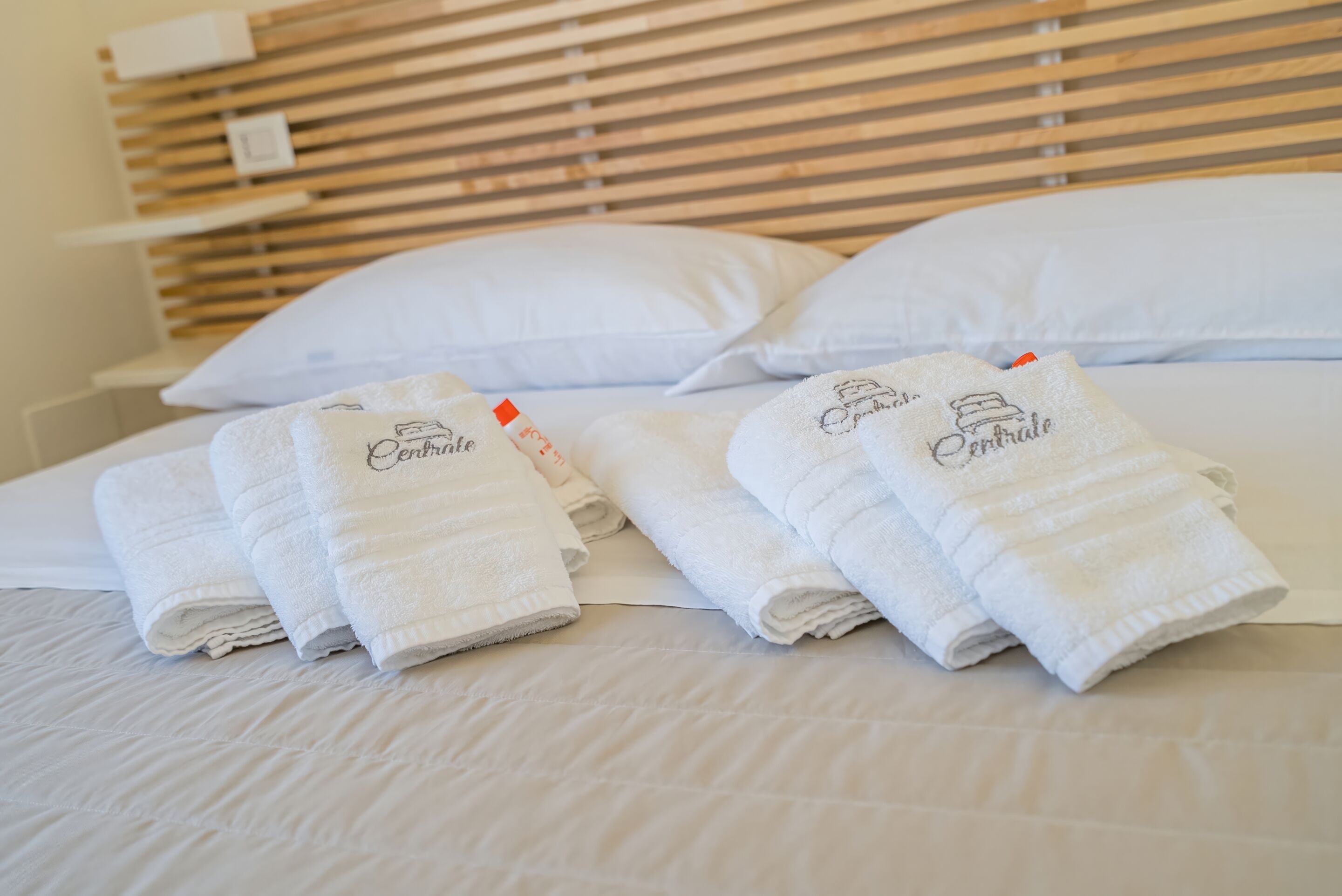 A neatly made bed with white linens and towels, a wooden headboard, and white pillows.