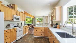 A modern kitchen with wooden cabinets, a white countertop, and a large window providing a view of the outdoors. - Cozy River Cabin - Sleeps 12 - Hot Tub - EV - Trails & Stevens Pass Nearby (Gold Bar)