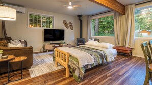 A cozy bedroom with a bed, a TV, a fireplace, and a large window with curtains. - Cozy River Cabin - Sleeps 12 - Hot Tub - EV - Trails & Stevens Pass Nearby (Gold Bar)