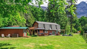 A two-story cabin with a deck, outdoor seating, and a barbecue area. - Cozy River Cabin - Sleeps 12 - Hot Tub - EV - Trails & Stevens Pass Nearby (Gold Bar)