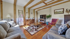 A spacious living room with wooden beams, a dining table with a patterned rug, and a cozy seating area with two sofas.
