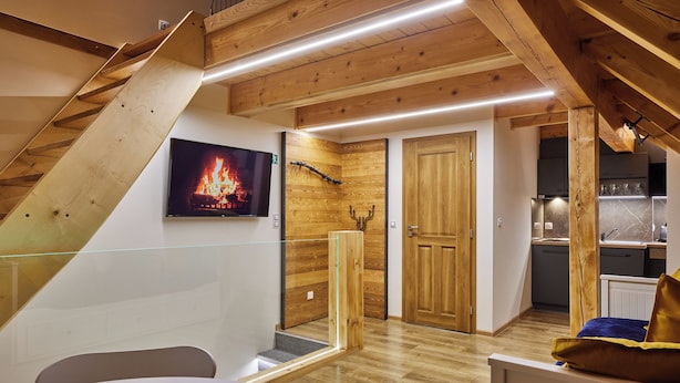 Ein modernes Interieur mit einer Holztreppe, einem Essbereich, einem Fernseher, der einen Kamin zeigt, und einer Küche.
