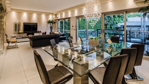 Una sala de estar moderna con una mesa de comedor de vidrio, asientos cómodos, un televisor grande y un balcón con vistas.
