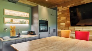 Une cuisine moderne avec une table en bois, des appareils électroménagers intégrés et un téléviseur fixé au mur.