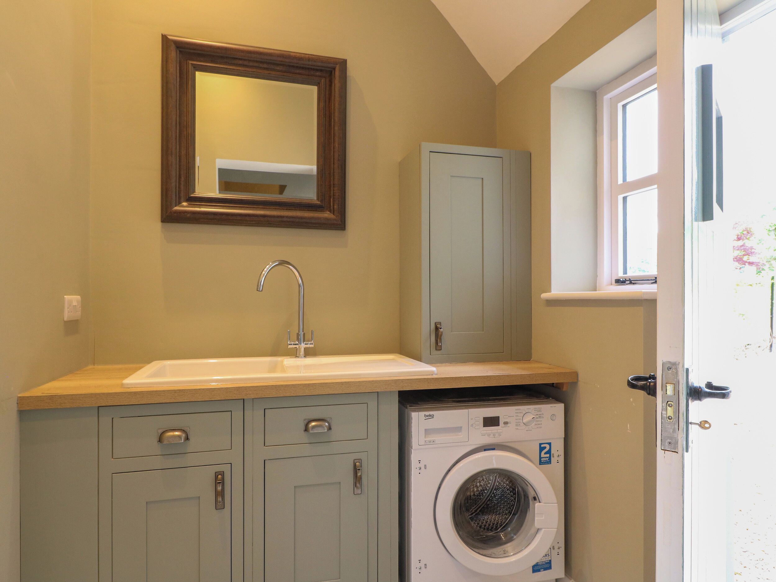 A compact bathroom with a sink, mirror, cabinet, and a front-loading washing machine.