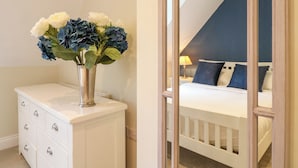Ein Schlafzimmer mit weißem Schminktisch, einem Spiegel und einem Bett mit blauer Bettwäsche.