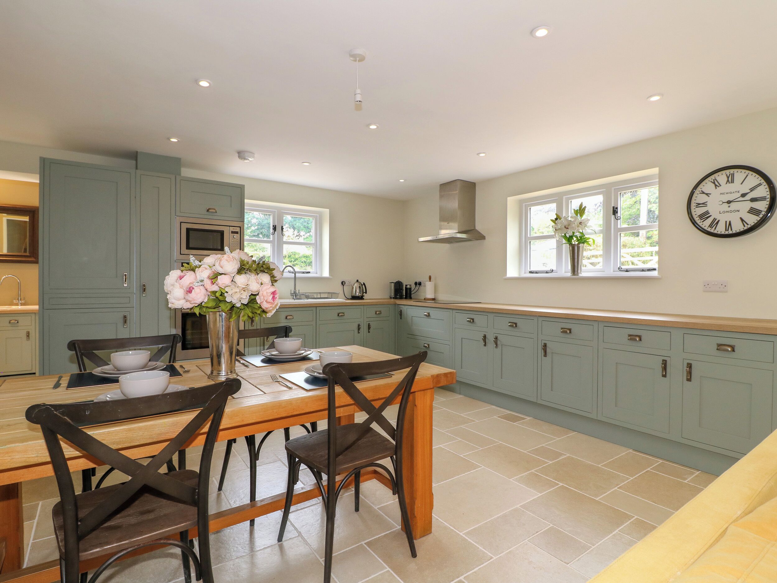 A kitchen with teal cabinets, a wooden dining table, and a wall clock.