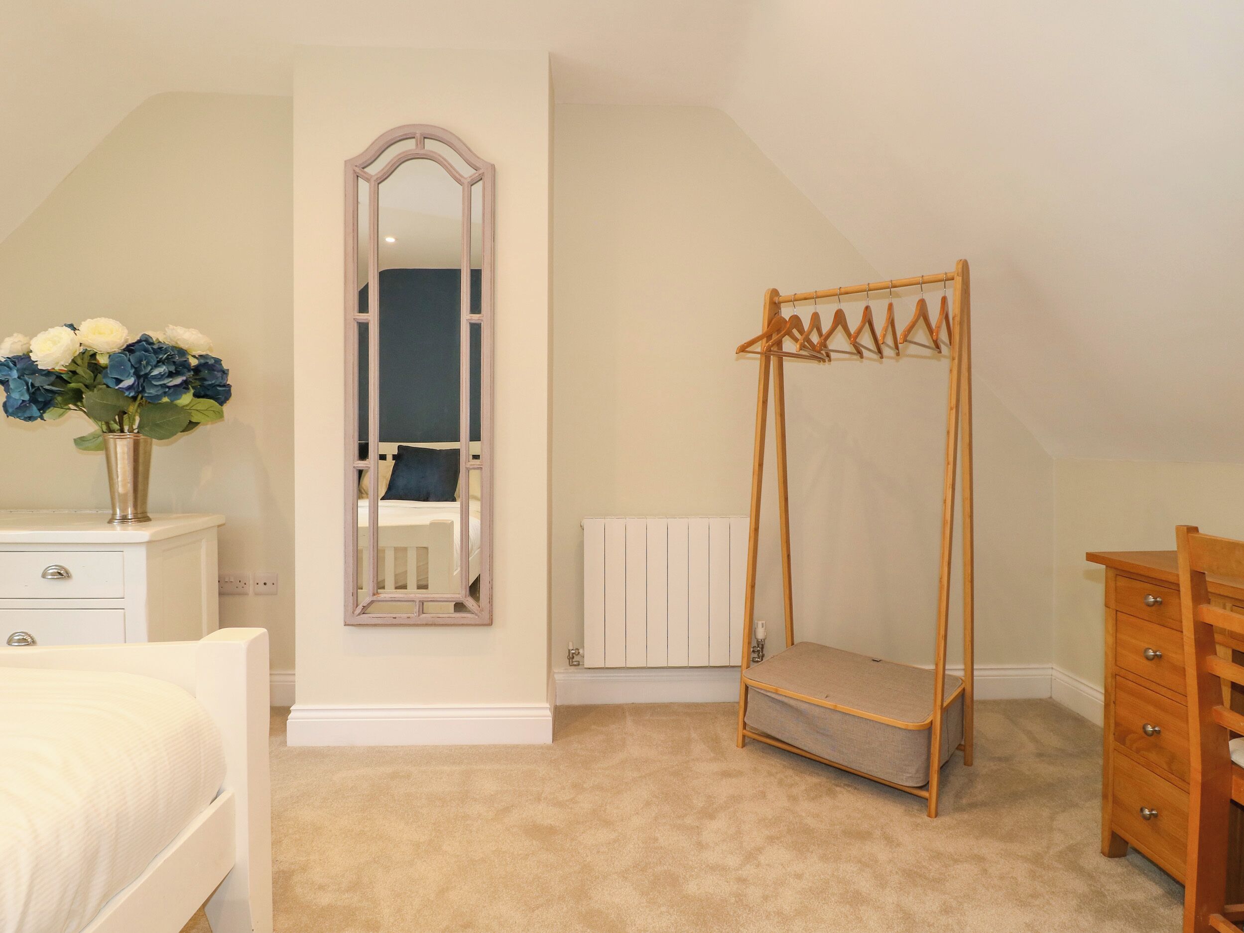 Un dormitorio con cama, cómoda, espejo, radiador y un tendedero de madera.