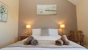 A neatly made bed with two rolled towels, two bedside lamps, and a painting on the wall. - Partridge Cottage (Filey)