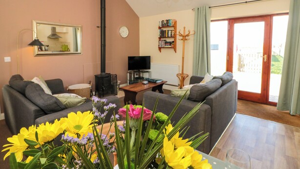 A living room with two sofas, a TV, a bookshelf, and a large window. - Partridge Cottage (Filey)