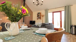 A dining area with a table set for two, a vase with flowers, and a chandelier. - Partridge Cottage (Filey)