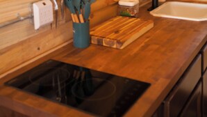A wooden kitchen with a built-in sink, a hanging utensil rack, and a cutting board on the counter. - Vintage Sheriff Tiny Cabin - HOT TUB! (Woodland Park)