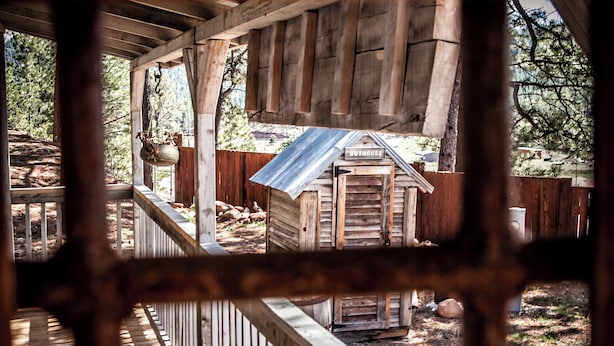 A rustic wooden structure with a porch and a small shed labeled "OUTHOUSE". - Vintage Sheriff Tiny Cabin - HOT TUB! (Woodland Park)