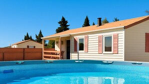 A swimming pool with a tiled deck, a house with a red roof, and a wooden fence in the background. - Coastal Bloom Pool & Garden Stay  (Conil de la Frontera)