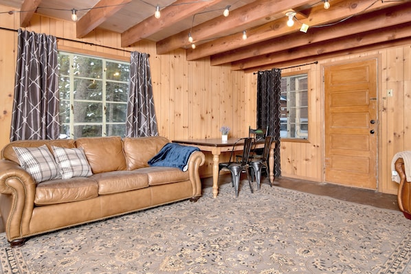 A cozy room with a brown leather sofa, a dining table with chairs, and a patterned rug.