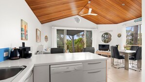 A modern kitchen with a central island, a dining area with a table and chairs, and a view of the outdoors. - Sails One - Inverloch (Inverloch)