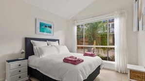 A bedroom with a bed, a nightstand, a window with curtains, and a framed picture on the wall. - Sails One - Inverloch (Inverloch)