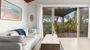 A living room with a grey sofa, a coffee table, and a large window with a view of the outdoors. - Sails One - Inverloch (Inverloch)