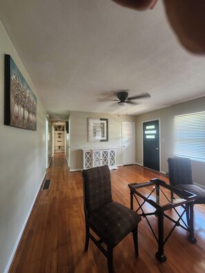 A spacious living room with hardwood flooring, a ceiling fan, and a view of the outside through a window with blinds. - Charming brick ranch on 1.28 acres near downtown Covington, GA, (Covington)