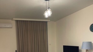 A modern living room with a sofa, a dining table, a TV, and a lamp. - Charming 1-bedroom apartment in delightful Batumi with AC, WiFi (Batumi)