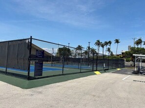Enjoy a game of tennis on the outdoor court, surrounded by a chain-link fence and shaded seating area.
