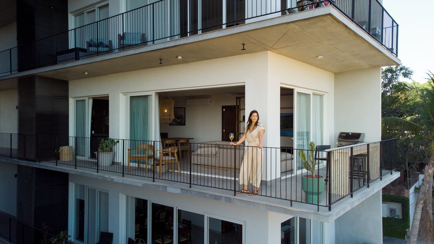 A modern two-story residential building with a balcony, outdoor seating, and a visible kitchen area.