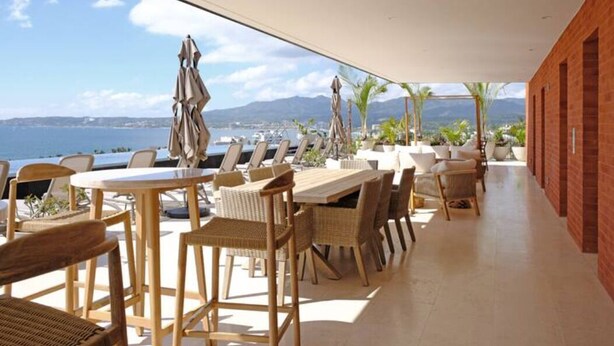 Une terrasse avec des tables et des chaises, une vue sur la mer et un mur en briques.