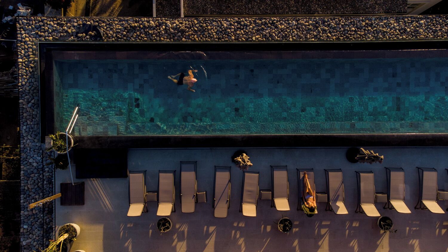 Una piscina de aguas cristalinas, rodeada de sillas de descanso y un borde de piedras.